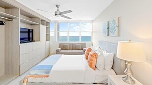 Een moderne hotelkamer met een groot bed, een televisie, een plafondventilator en uitzicht op zee.
