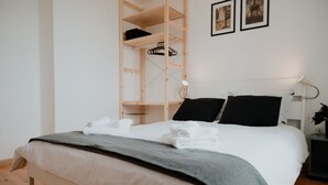 Un letto rifatto con lenzuola bianche e grigie, una testiera in legno e un comodino con una lampada.