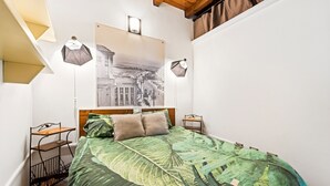 Ein Schlafzimmer mit einem Bett, einem Nachttisch, einem Wandregal, einem gerahmten Bild und einer Pendelleuchte.