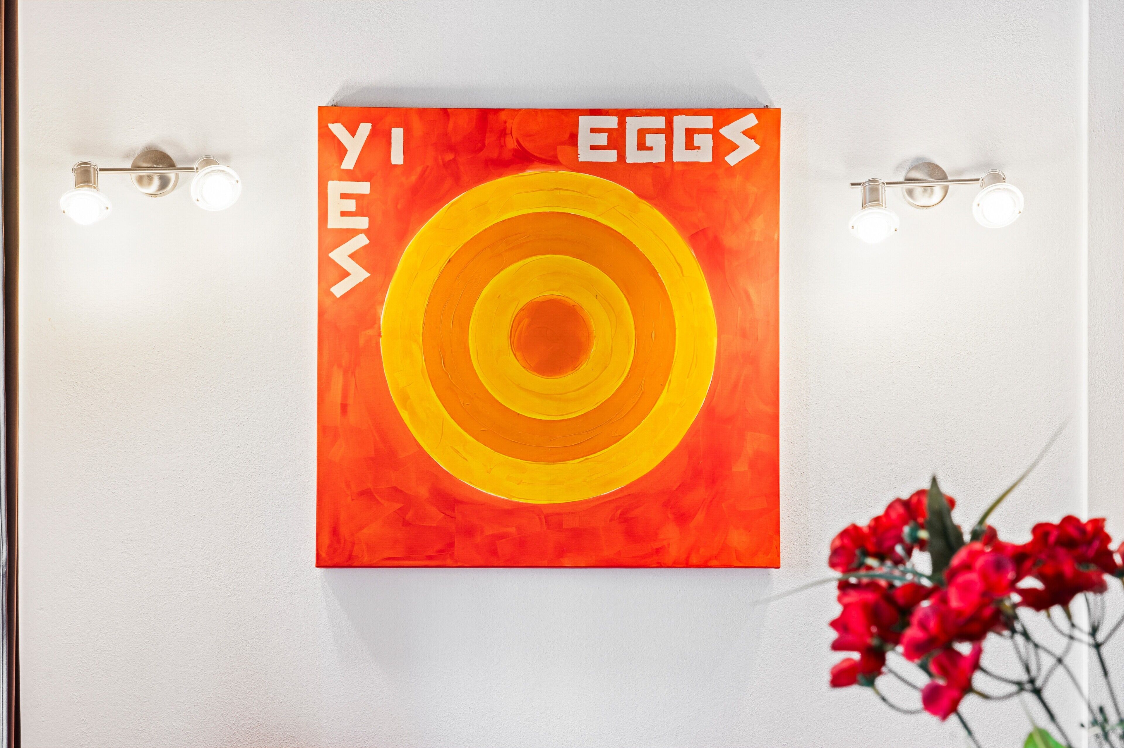 A wall with a colorful artwork featuring concentric circles and the text 'YES EGGs'.