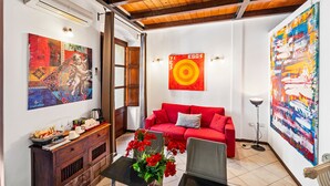 Ein Wohnzimmer mit einem roten Sofa, einem Couchtisch mit Blumen, einem Bild an der Wand und einem großen abstrakten Gemälde.