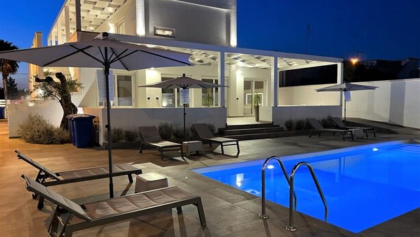Una casa moderna amb piscina, zona d'estar a l'exterior i un pati ben il·luminat.