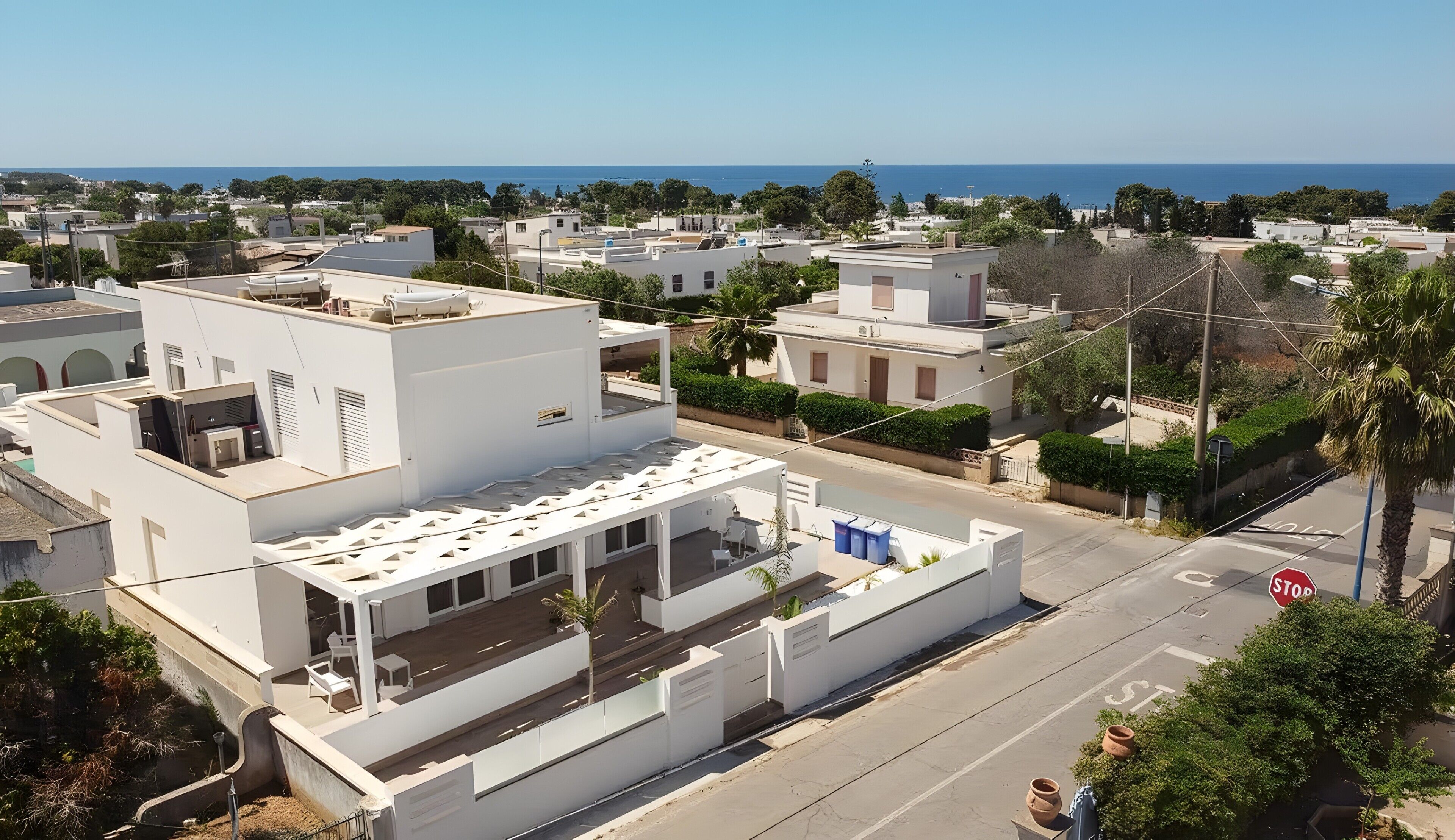 Un quartier résidentiel avec des bâtiments blancs, une rue avec un panneau de signalisation indiquant un arrêt obligatoire, et une vue sur la mer.