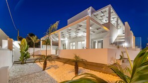 Un edifici modern amb una zona exterior coberta, parets blanques i un camí de grava.