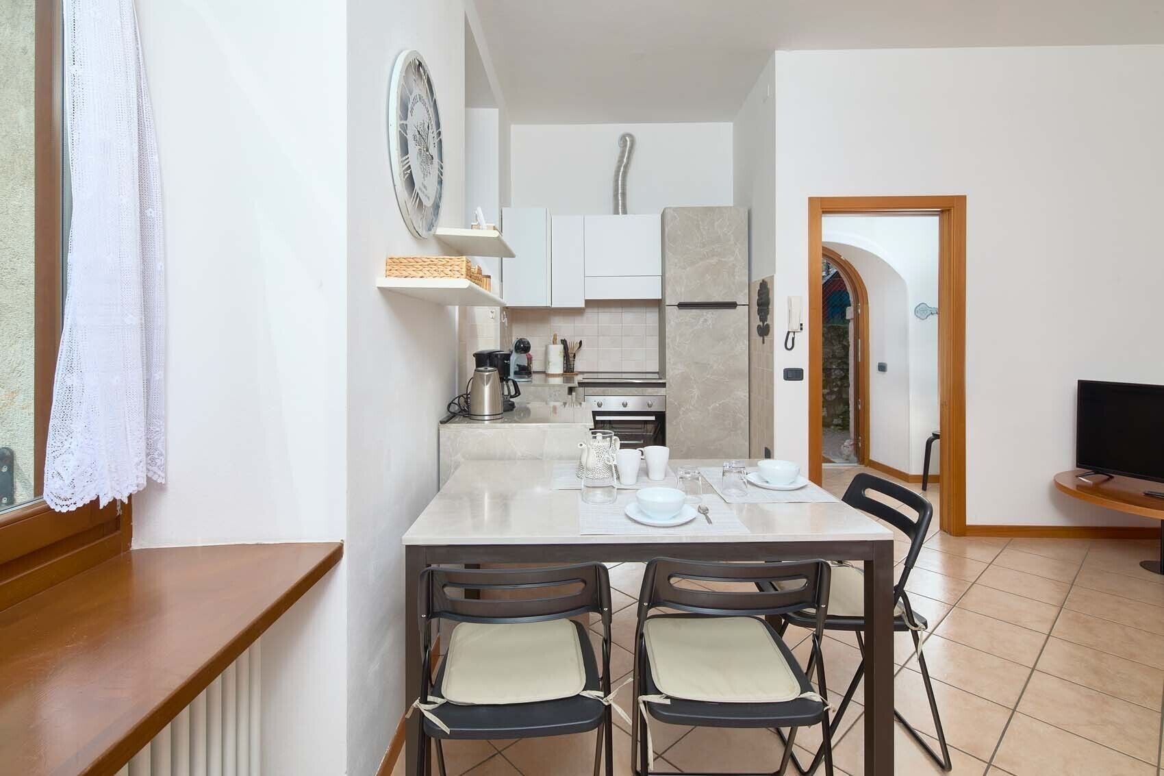 Una cocina compacta con zona de comedor, que incluye una mesa dispuesta para cuatro personas, un refrigerador y una cafetera.