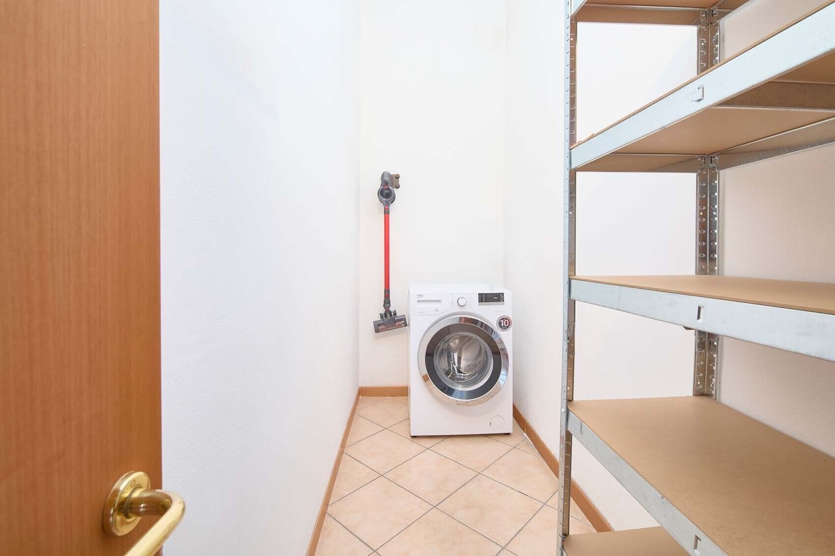 Une buanderie équipée d’un lave-linge, d’étagères et d’une porte.