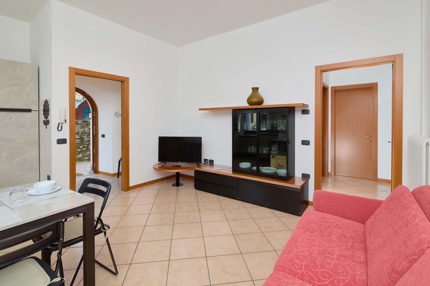 A living room with a TV, a glass cabinet, a dining table with chairs, and a red sofa.