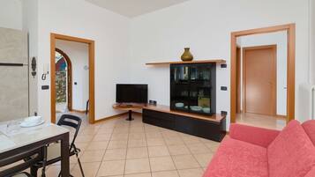 A living room with a TV, a glass cabinet, a dining table with chairs, and a red sofa.