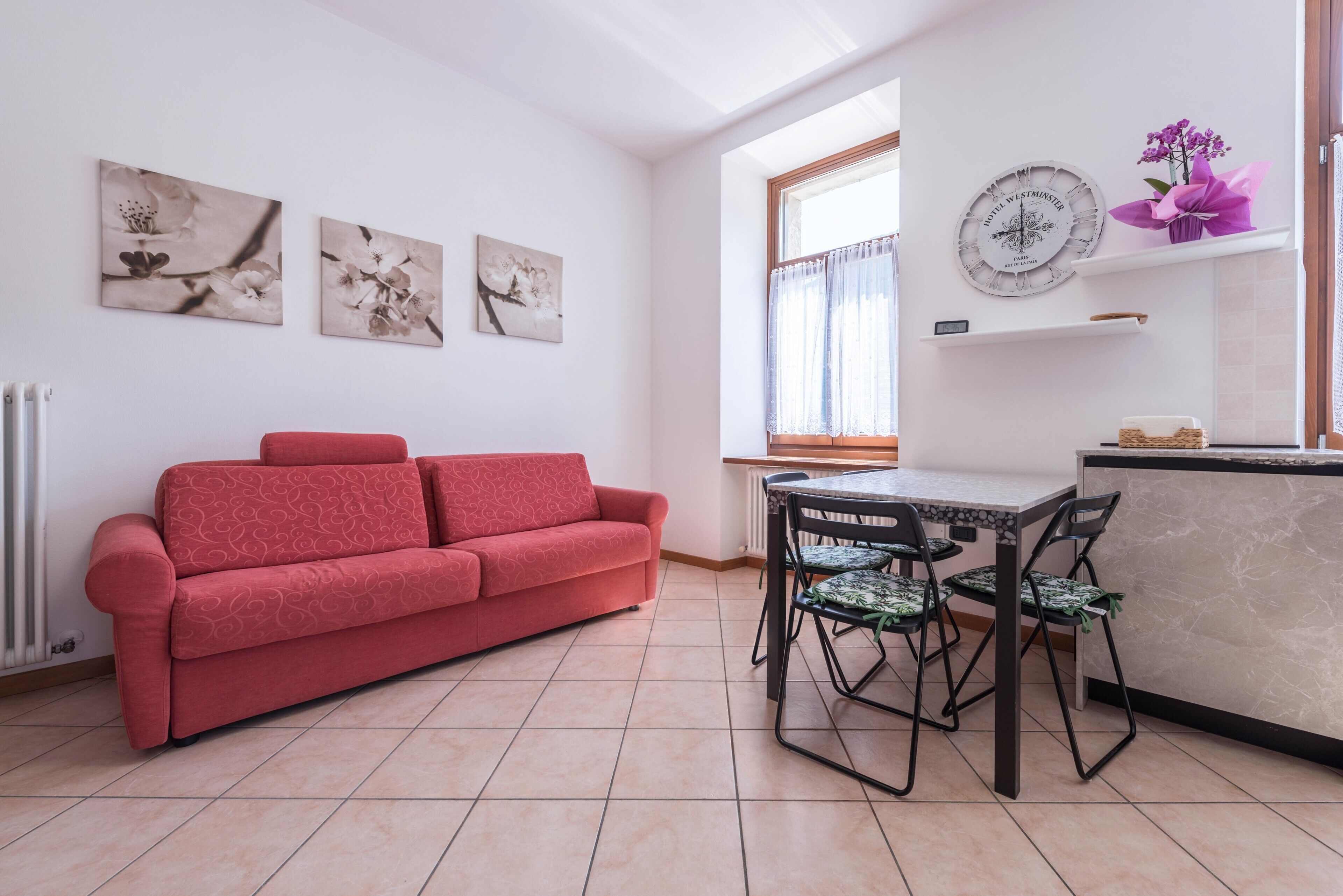Un canapé rouge, une table à manger avec des chaises, une horloge et des œuvres d’art accrochées au mur.