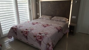 A bedroom with a bed, a nightstand, a wall-mounted light, and a window with blinds.