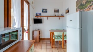 A compact kitchen with a microwave, a refrigerator, a wooden table, and a television mounted on the wall. - Holiday Home ‘Residenza Solemar - App 14’ with Sea View, Wi-Fi (Bosa Marina)