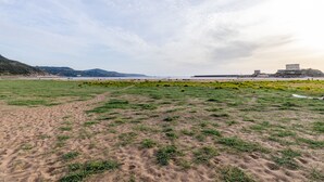 A coastal landscape with a sandy beach, grassy areas, and a distant building on a hill. - Holiday Home ‘Residenza Solemar - App 14’ with Sea View, Wi-Fi (Bosa Marina)