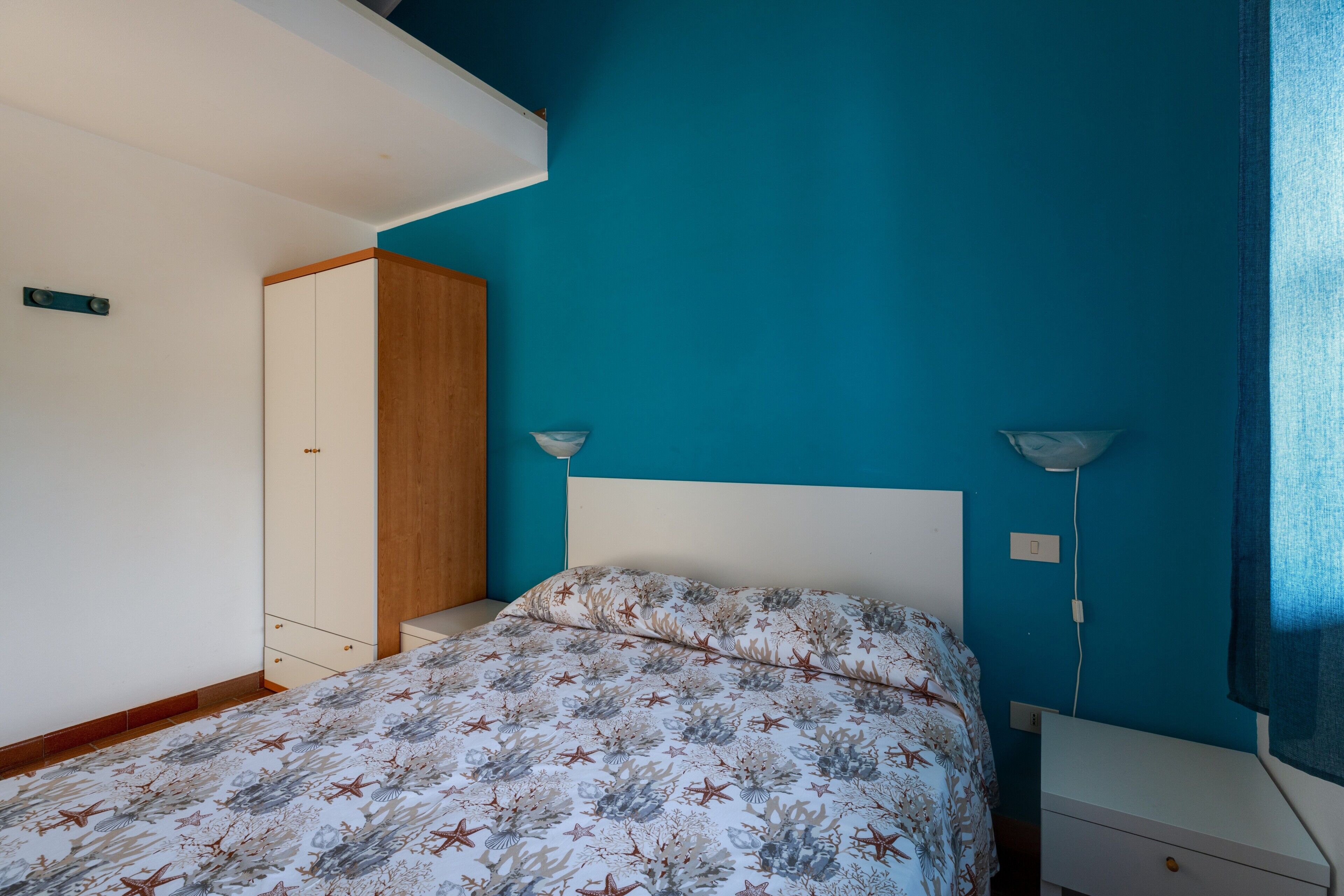 A bedroom with a bed, a wardrobe, a bedside table, and a lamp.