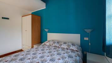 A bedroom with a bed, a wardrobe, a bedside table, and a lamp.