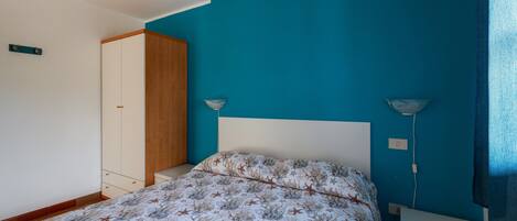 A bedroom with a bed, a wardrobe, a bedside table, and a lamp.