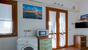 Une pièce comprenant un lave-linge, une armoire avec des tiroirs, un téléviseur posé sur un meuble et un tableau accroché au mur.