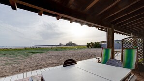 An outdoor patio with a table and chairs, overlooking a beach and a distant building.