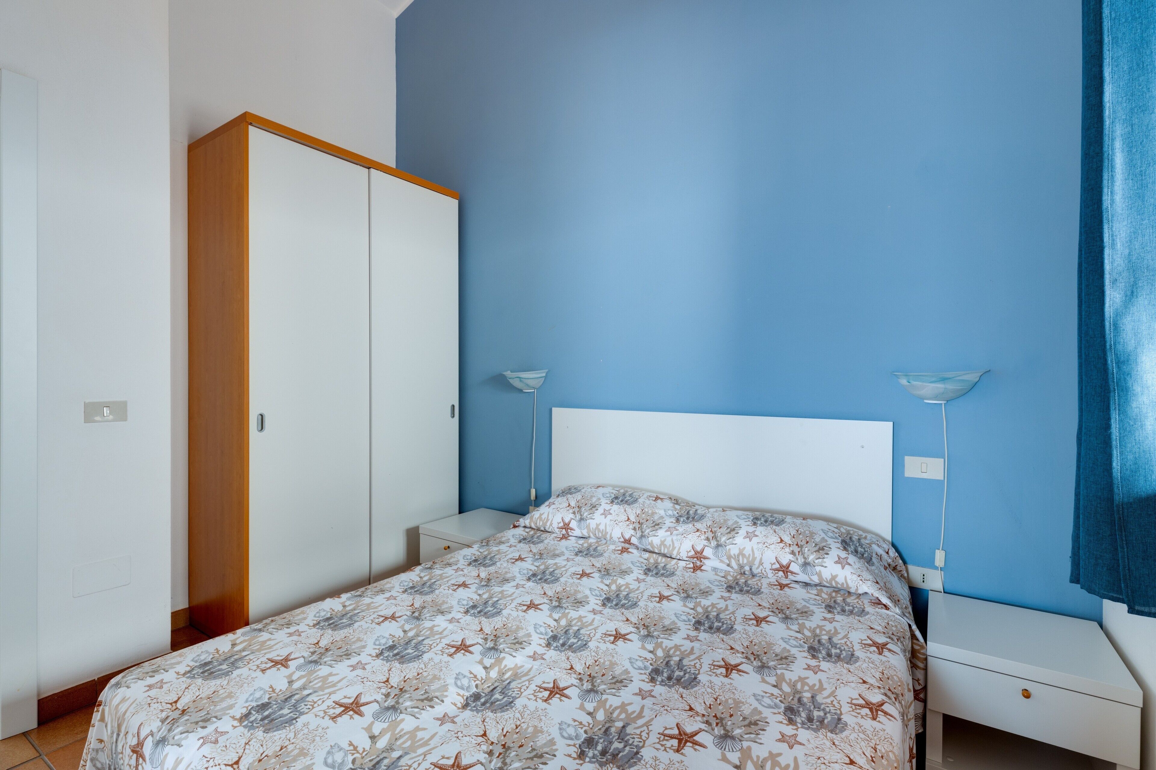 Ein Schlafzimmer mit einem Bett, Nachttischen, einem Kleiderschrank und einer blauen Wand.