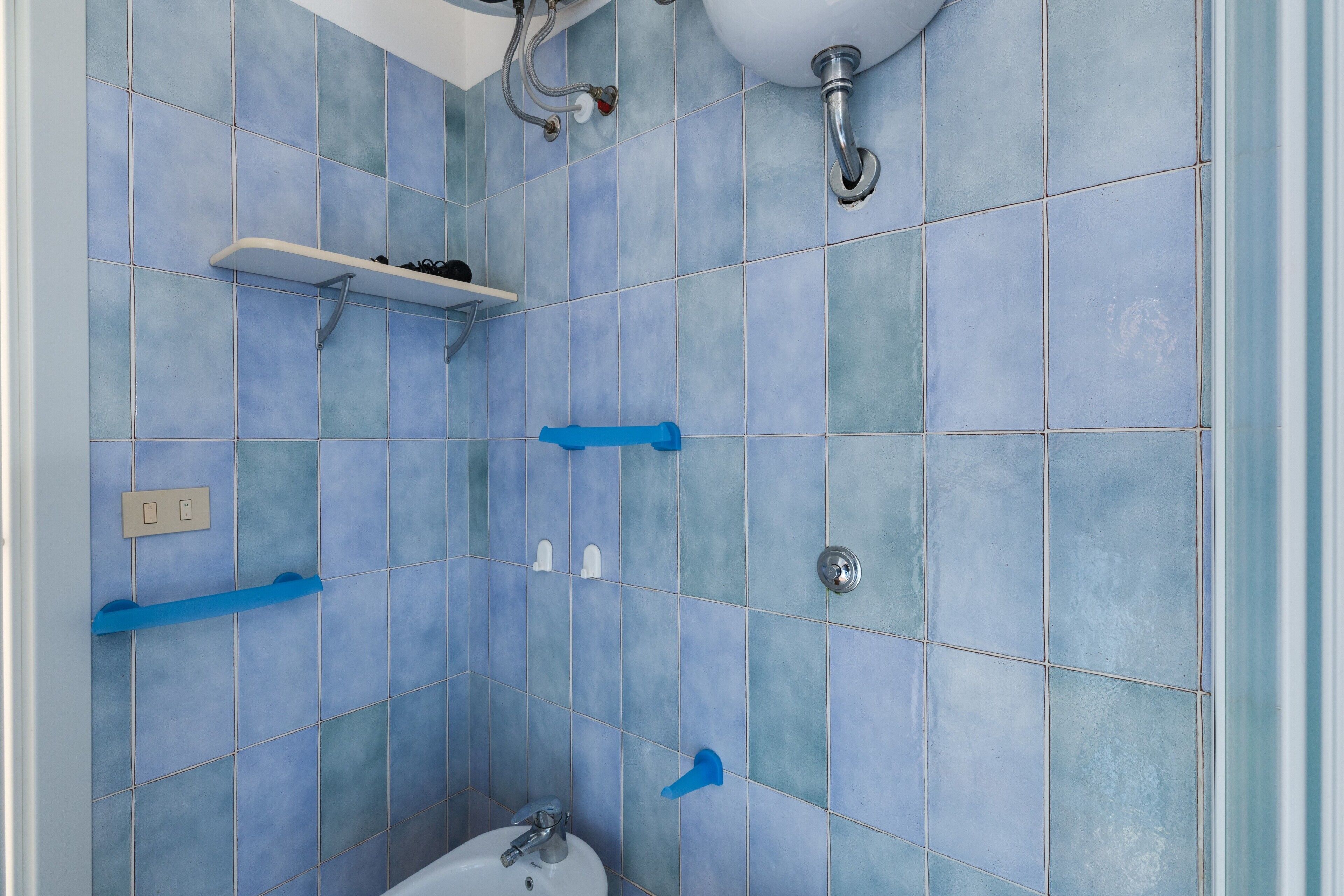 Un baño con azulejos azules, un lavamanos blanco, una repisa y una zona de ducha.
