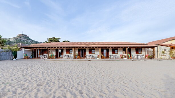 A building with a tiled roof, a flat entrance, and a sandy ground.