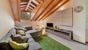 Una sala moderna con techo inclinado, un conjunto de sofás, un televisor y un reloj en la pared.