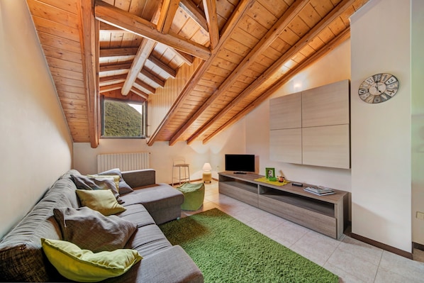 A modern living room with a sloped ceiling, a sofa set, a TV, and a clock on the wall.
