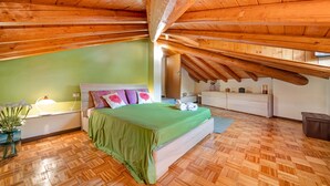 Un dormitorio con techo de madera, una cama con colcha verde, una mesita de noche, una lámpara y un aparador.