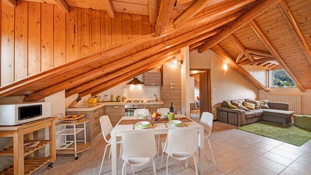 Un loft moderno con vigas de madera a la vista, una cocina con electrodomésticos blancos, una zona de comedor con sillas blancas y un espacio de estar con un sofá.