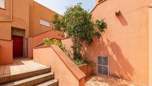 Un escalier menant à une porte, une plante en pot et un mur avec une grille d’aération.