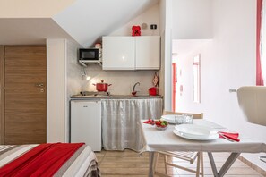 A compact kitchen with a microwave, stove, and small refrigerator. A dining table with plates and cutlery is set for two.