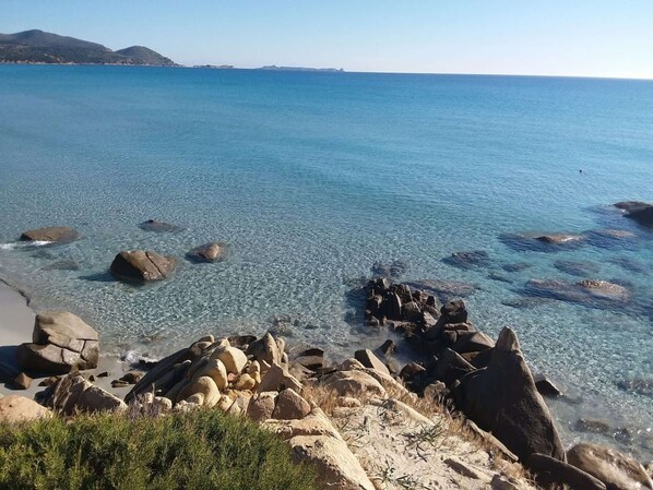 A coastal landscape with clear water, rocks, and distant hills.