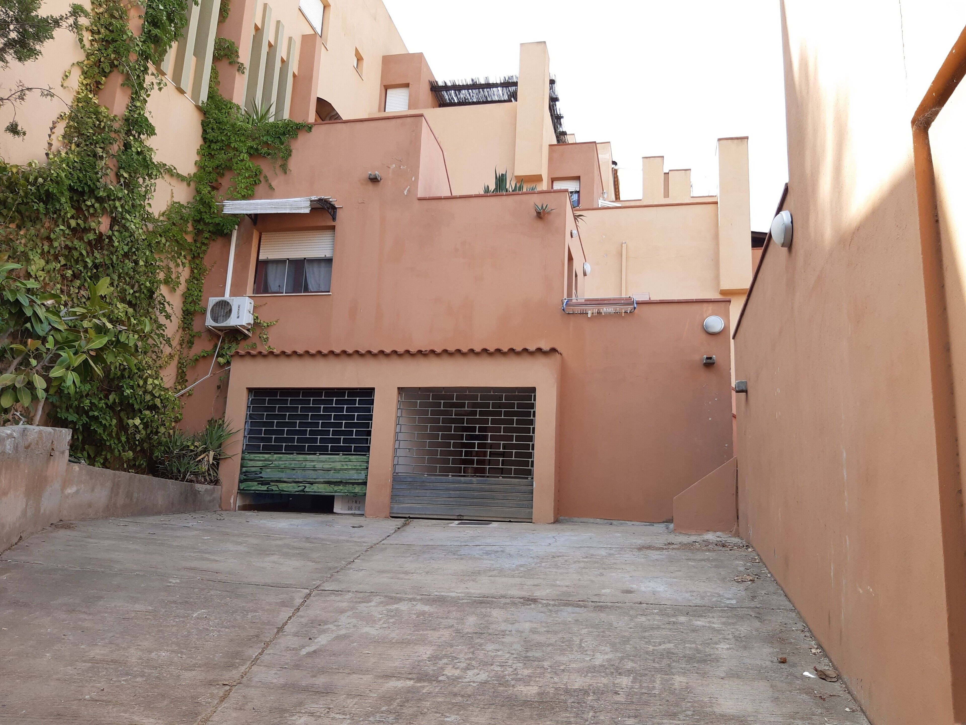 Une ruelle étroite avec un bâtiment dont la façade comprend une porte de garage en briques, une petite fenêtre et un appareil de climatisation.