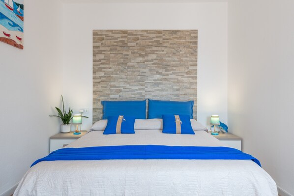 Ein ordentlich bezogenes Bett mit blauer und weißer Bettwäsche, ein Kopfschild mit Steinmuster und Nachttischlampen.