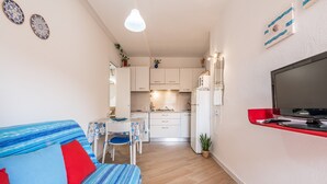 A compact living space with a sofa, dining table, kitchenette, and a TV mounted on the wall.