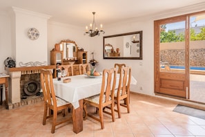 Un espace repas comprenant une table, des chaises, un lustre, une cheminée, un miroir et une vue sur une piscine.