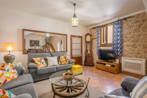 Un salon avec un canapé, une table basse en verre, un téléviseur, une horloge et un mur en pierre.