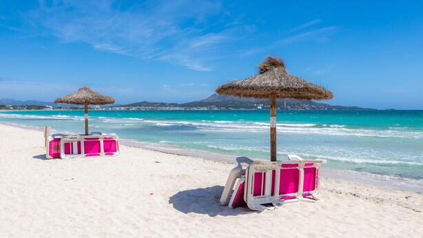 A beach with thatched umbrellas and pink beach chairs on the sand. - Chalet Villa Can Jaume with Wi-Fi, A/C, Terraces & Garden; Pet-Friendly (puerto alcudia)