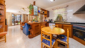 A kitchen with wooden cabinets, a dining table with chairs, a built-in oven, and a large window with curtains. - Chalet Villa Can Jaume with Wi-Fi, A/C, Terraces & Garden; Pet-Friendly (puerto alcudia)