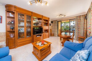 Una sala de estar con televisor, armarios de madera, un sofá y un comedor con mesa y sillas.