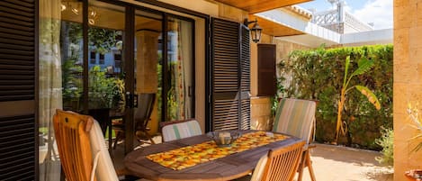 An outdoor dining area with a wooden table and chairs, a chessboard, and a potted plant.