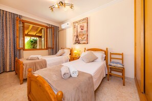 Une chambre d’hôtel avec deux lits en bois, une chaise en bois, une fenêtre avec des rideaux, une lampe fixée au mur et une affiche de la Tour Eiffel.