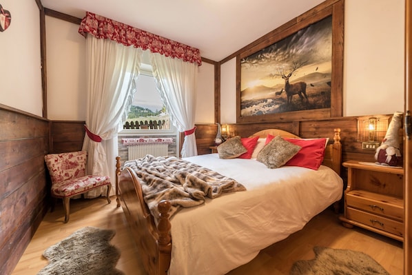Une pièce aux murs lambrissés, comprenant un lit, une chaise, un tableau et une fenêtre avec des rideaux.