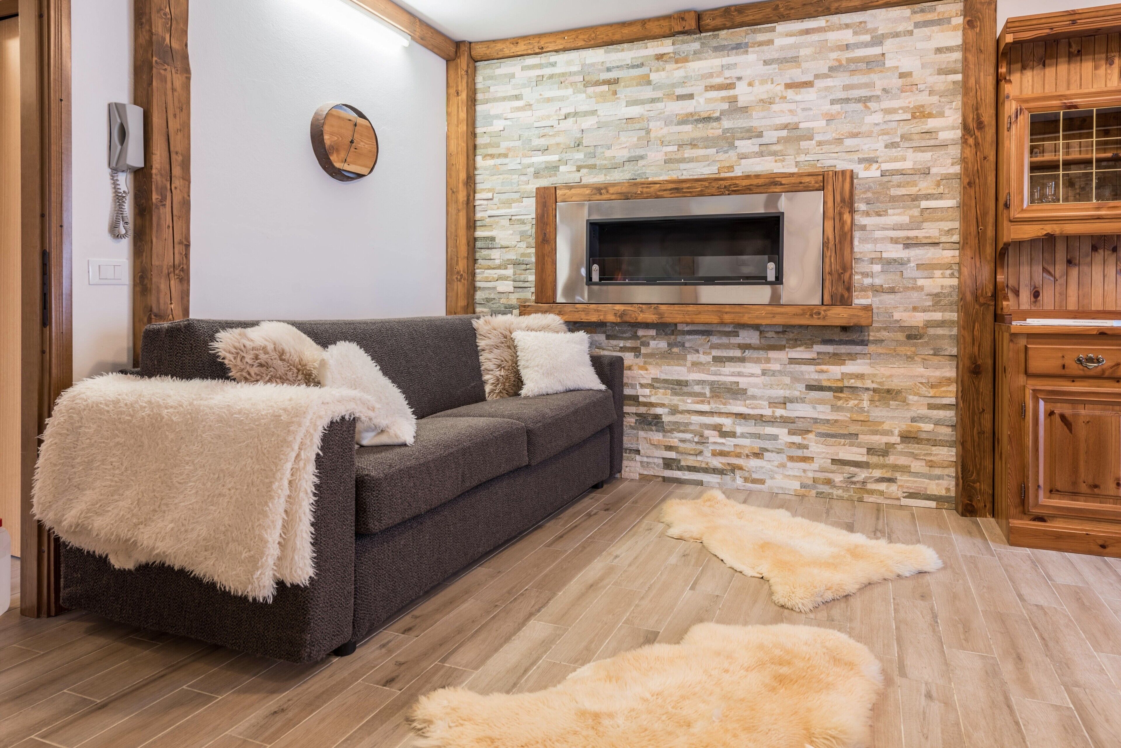 Una sala de estar moderna con una pared de piedra, televisor integrado, un sofá oscuro y armarios de madera.