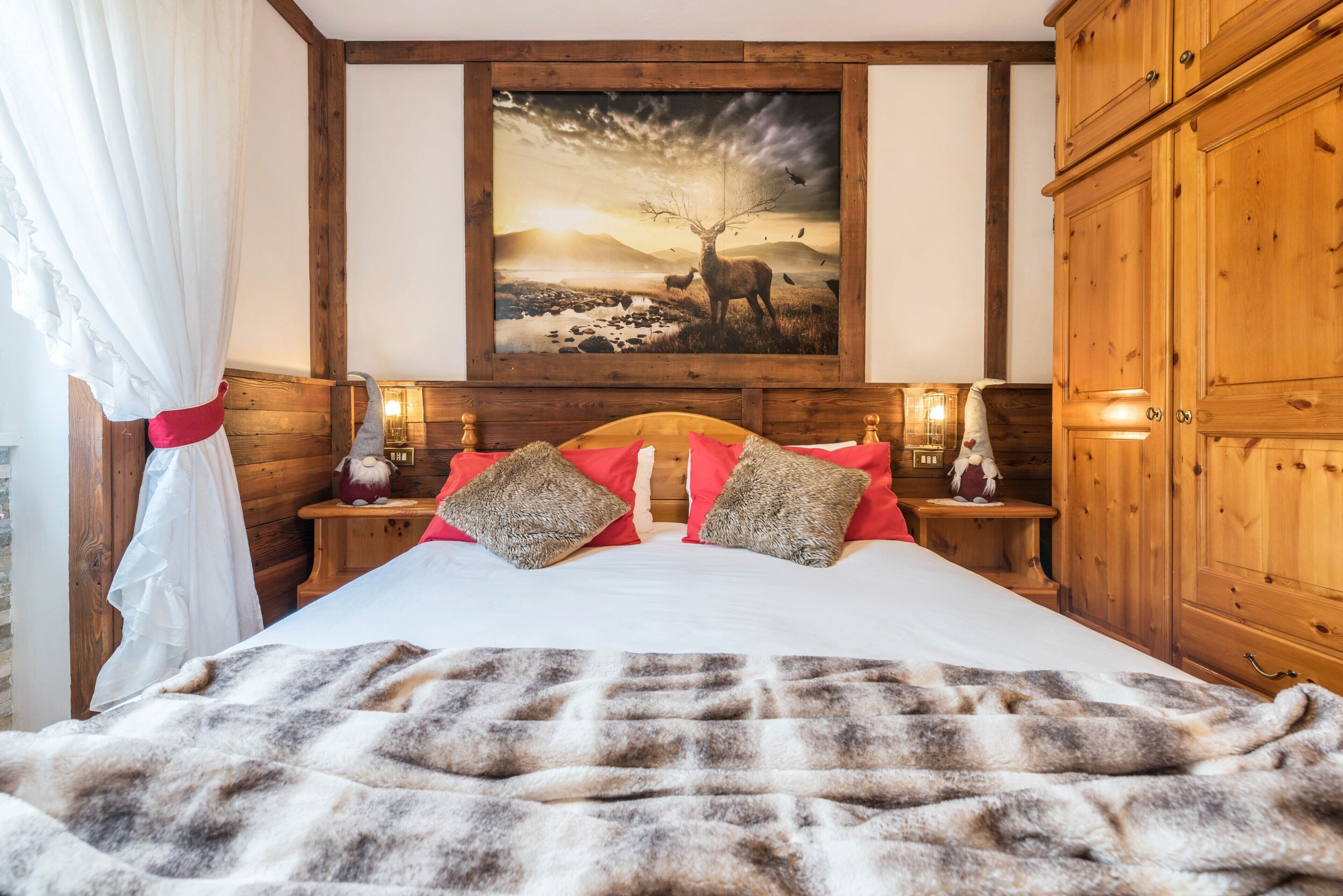 Une pièce aménagée comme une cabane en bois, avec un grand lit, un tableau représentant un cerf et des armoires en bois.