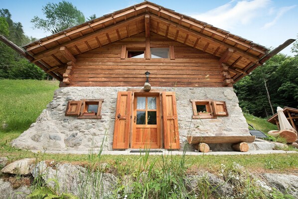 Une cabane en rondins avec une base en pierre, des volets en bois et un toit à deux versants.