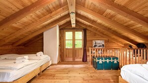 Een houten blokhut met een slaapkamer op een entresol, een houten vloer en een hoger gelegen slaapplek.