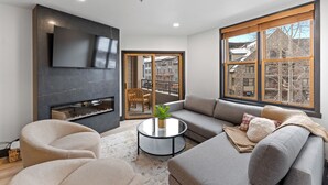 A modern living room with a fireplace, a large flat-screen TV, a sofa, and a coffee table. - Silver Mill #8162 by Summit County Mountain Retreats (Keystone)