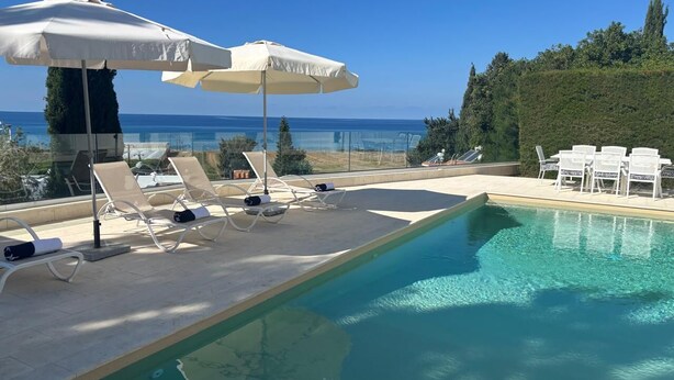 Zona de piscina amb gandules i ombrel·les, vista despejada al mar i piscina ben cuidada.