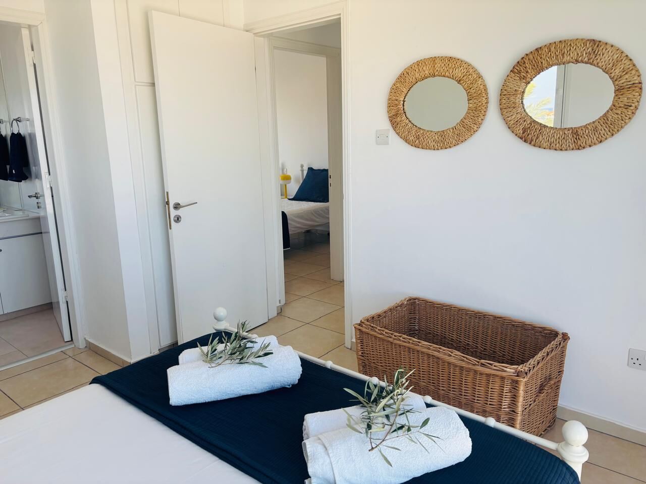 Une chambre à coucher avec un lit, deux miroirs ronds, un panier en osier et une porte donnant sur une autre pièce.