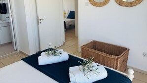 Un dormitori amb un llit, dos miralls rodons, una cistella de vimet i una porta que condueix a una altra habitació.